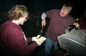 Slug: NBRE genoa13p        Date:   11/07/2008       The Blade/Andy Morrison       Location:  Fremont      Caption: Lisa Mullen, left, a teacher at Brunner Elementary School in Genoa, gets a hamburger from Genoa fan Dave Marko as they and others tailgate before the Comets play Fostoria High School at Don Paul Stadium in Fremont, Friday, 11/07/2008.         Summary: