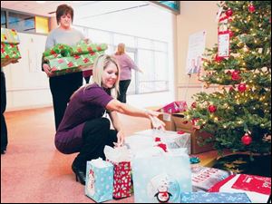 From left, employees Stephanie Babbitt, Laura Wester, and Courtney Wagner place gifts for needy families under a tree at Owens Corning headquarters.