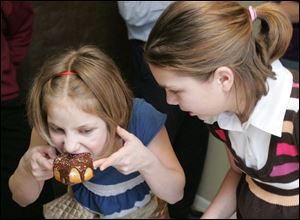 Miriam Shafransky, 10, eats a fried doughnut as Halie Johnstone, 11, observes, after a performance of  Maccabees. 