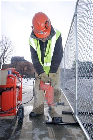 Scott Easterwood, an employee of Rudolph-Libbe, drills brackets for a fence at Superior and Jackson streets in downtown Toledo, site of the United Way s new headquarters. The six-foot-high chain-link fence put up yesterday was the first visible sign that a new United Way headquarters will be erected in the shadow of the old building. The Toledo Plan Commission in November gave its OK for work on the building to proceed.