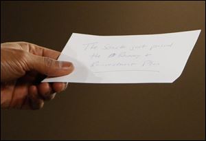 President Obama holds a note with the words 'The Senate just passed the Recovery and Reinvestment Plan,' in reference to the economic stimulus package, after it was passed to him by aide Reggie Love, not pictured, while Obama was on stage during a town hall meeting to discuss the economy Tuesday.