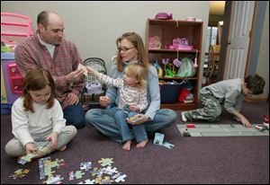 Perrysburg Township firefighter Chad Merrick relaxes with his family in their Perrysburg home by helping the children with their games. From left are Keely, 5; Ailey, 2, on the lap of her mother, Kristen, and Aidan, 8.
