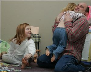 Keely, 5, and Ailey, 2, give attention to their dad, cancer survivor Chad Merrick, at family time in their Perrysburg home.