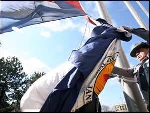 Trooper Mike Rodriguez of the Ohio Highway Patrol battles the wind as he raises two new flags in front of Government Center in downtown Toledo. Snow is forecast for today, with accumulations of 2 to 4 inches before it tapers to flurries this afternoon. 