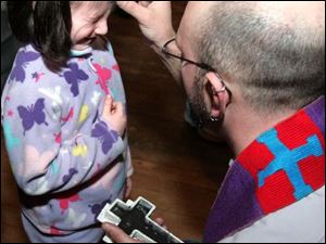 Lilly Stuart winces as ashes are applied to her forehead yesterday by her father, the Rev. Will Stuart, pastor of Nu-Vizion United Church of Christ, 2014 Cherry St., during its Ash Wednesday service. Ash Wednesday marks the beginning of the 40-day season of Lent leading up to Easter, and the ashes are meant to serve as reminders of human beings  mortality.