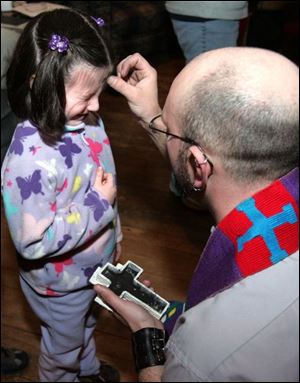 Lilly Stuart winces as ashes are applied to her forehead yesterday by her father, the Rev. Will Stuart, pastor of Nu-Vizion United Church of Christ, 2014 Cherry St., during its Ash Wednesday service. Ash Wednesday marks the beginning of the 40-day season of Lent leading up to Easter, and the ashes are meant to serve as reminders of human beings  mortality.