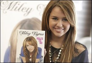 inger and actress Miley Cyrus poses with a copy of her book 