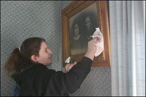 Rebekah Titus wipes dust from a picture in the 1910 farmhouse at Sauder Village. Almost 60 students volunteered at the historic site.