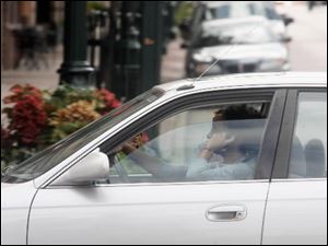 A motorist talks on a hand-held cell phone as she travels on East Wooster Street near Main Street in Bowling Green. Voters are being asked to outlaw such behavior.