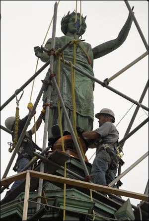 Workers secure the base of the statue, which had spent the winter undergoing 'copper cosmetology.' It had been riddled with bullet holes and was missing some key parts. The restoration cost $22,050, largely paid for with donations.