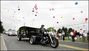 A motorcycle pulls the hearse with the body of Nevaeh Buchanan along the route of the funeral procession Saturday as balloons are released.