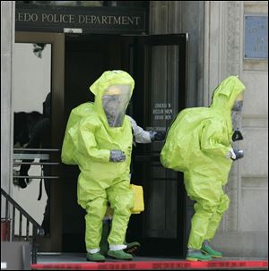 Members of the Toledo Fire Department in protective gear leave the Safety Building downtown after a box containing an unknown white powder was unknowingly opened by police officers yesterday afternoon. Tests showed the substance was harmless. 