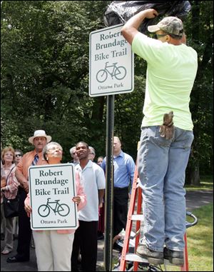 Councilman Wilma Brown watches as city worker Joe Tarejlis unveils the sign dedicating the bike trail at Ottawa Park to Robert Brundage, an avid bicyclist.