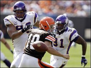 The Browns' Brady Quinn scrambles and loses the ball behind him as Kevin Williams, left, and Ray Edwards close in. The Vikings recovered and pulled away in the second half.