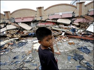 A boy stands in front of a flattened building in Padang, Indonesia, where workers are still pulling people from under the rubble.