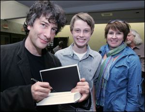 Author Neil Gaiman signs one of his books for Derek Kastner and his mom, Kim Kastner, of Sylvania. The author said the words, So what happened next? made him finish 'The Graveyard Book.'