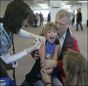 Craig McKee of Ann Arbor holds daughter Regan, 6, as she is vaccinated by nurse Diane Krill, assisted by Amy Jones, at the Bowling Green clinic. Laws prohibit officials from turning people away at free clinics, even if they're from outside the county.