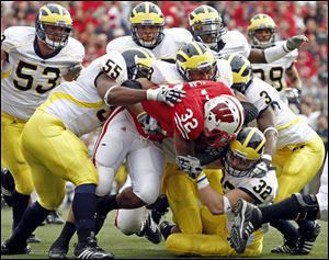 Wisconsin's John Clay, who rushed for 151 yards on 26 carries, is brought down by Michigan defenders, including Brandon Graham (55) and JordanKovacs (32), a Clay graduate.