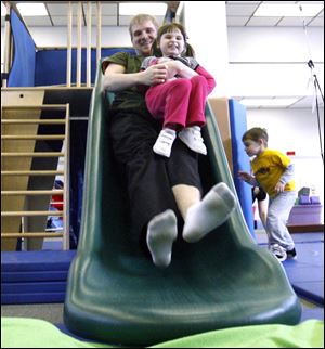 Intern Andrew Schoene accompanies Luke Lyons' twin, Lily, down a slide.