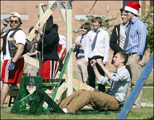 Larry Jajou, seated, and other physics students at St. Francis de Sales High rejoice after he successfully launched a canned good from a catapult outside the school. The project Monday was intended to illustrate physics principles.