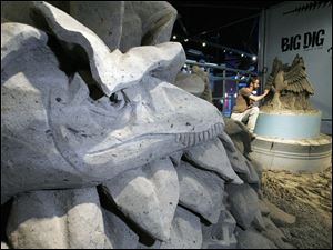 A stegosaurus munches on foliage as it eyes Mr. Jara, working at right. The sand sculpture of prehistoric life is part of Imagination Station's newest exhibit, ‘The Big Dig.'