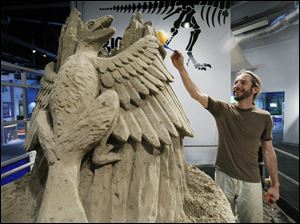Carl Jara works on an archaeopteryx — a Jurassic Period reptilian bird — as part of a 25-ton sand sculpture at the Imagination Station. The reigning world-champion sand sculptor is to finish the piece for Thursday night's Members Event at the science center.