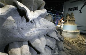 A stegosaurus munches on foliage as it eyes Mr. Jara, working at right. The sand sculpture of prehistoric life is part of Imagination Station's newest exhibit, ‘The Big Dig.'