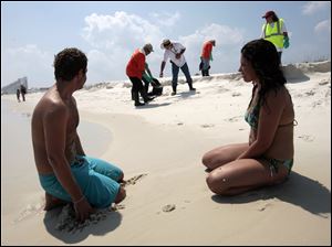Husband and wife Josiah and Lydia Holmes of Gulf Shores, Ala., sit on the beach in Perdido Key, Fla., and watch as an oil cleanup crew removes tar balls and bits of oil that have come ashore.