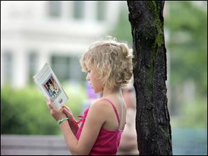 Maison Gargac, 8, of Crossville, Tenn., reads a Nancy Drew novel she'd just checked out of the Main Toledo-Lucas County Public Library downtown. Maison is in town visiting her grandparents while school's out and had enrolled in the library's summer reading program before checking out the book Wednesday. The program started this week and runs through Aug. 7.