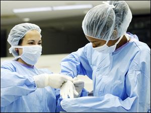 Toledoan Kayla Repass, left, helps Victoria Turnbough, also of Toeldo, into a pair of surgical gloves. 