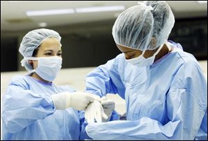 Toledoan Kayla Repass, left, helps Victoria Turnbough, also of Toeldo, into a pair of surgical gloves. 