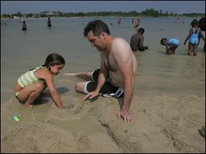 Mitch Crawford, a teacher on summer break from St. John's High School, plays in the sand Monday with his daughter Addison, 6, at Maumee Bay State Park.. 