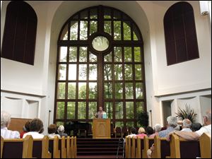 At First Seventh-day Adventist Church, the Rev. Mike Fortune speaks to the visitors as he stands before a 43-foot window that looks out on a lush patch of trees and Sylvania Avenue. 