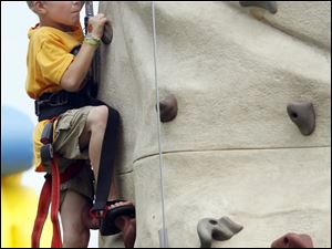 Harnessed for safety, 8-year-old Hunter Dillman grabs toe and hondholds as he tests his skills on a climbing wall at the Fun Fest.