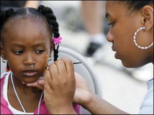 Talia Ulrich concentrates as she paints a design on the face of La'Nyah Foster, 3, during the Family Fun Fest.