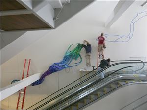 Workers begin the installation of the work, which is made from thousands of pieces of blue, green, and purple plastic.