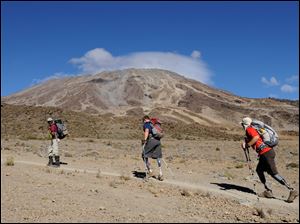 Local guide Godlisten Moshi leads Neil Duncan, 26, of Denver, center, and Dan Nevins, 37, of Jacksonville toward Mount Kilimanjaro in Tanzania.