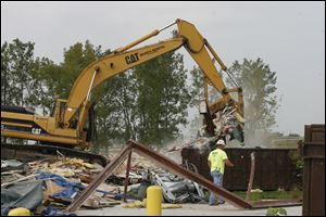 CTY demo12p  Shane Garlick operates an excavator to clear the site of the former Lake Township Administration Building. Lonie (cq) Featherstun, next to the dumpster, is sorting metal for recycling, so 