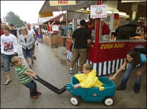 Slug: CTY pull22p C  The Blade/Jeremy Wadsworth  Caption:  Austin Reardon, 3, of Woodville, Ohio, pulls his brother Christopher Reardon, 5, with some help from his mom Sara Reardon while waiting for The National Tractor Pulling Championships to get started after a long rain delay Saturday, 08/21/10, in Bowling Green, Ohio. This is the world's largest outdoor pulling event. There are five sessions of premier truck and tractor pulling on two tracks featuring over 250 pullers competing in 11 different classes.