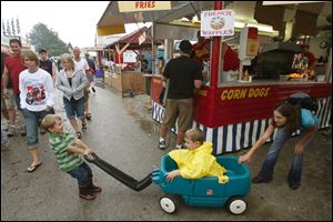 Slug: CTY pull22p C  The Blade/Jeremy Wadsworth  Caption:  Austin Reardon, 3, of Woodville, Ohio, pulls his brother Christopher Reardon, 5, with some help from his mom Sara Reardon while waiting for The National Tractor Pulling Championships to get started after a long rain delay Saturday, 08/21/10, in Bowling Green, Ohio. This is the world's largest outdoor pulling event. There are five sessions of premier truck and tractor pulling on two tracks featuring over 250 pullers competing in 11 different classes.