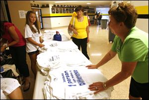 Abbey Pawlak, 13, left, and Dana Hooper, right, director of Glass City Volleyball Co., arrange T-shirts for sale a the charity volleyball game at Northview.