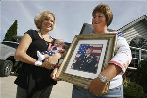 Alisha Reif, cradles 2-month-old daughter, Elena, as Sergeant Reif's mom, Carrie, proudly clutches a portrait of her warrior son. 