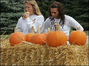 Crystal Venia munces on an apple as she and daughter Lauren, 16, both of Ottawa Lake, look over a clutch of pumpkins.