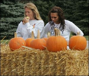 Crystal Venia munces on an apple as she and daughter Lauren, 16, both of Ottawa Lake, look over a clutch of pumpkins.