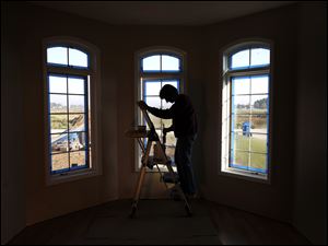 Carolyn Booth is framed in the window bay as she paints the dining room of a house under construction on Tournament Drive in Monclova Township.