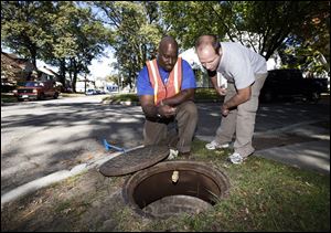 Vaughn Jackson, left, and Brian Hahn, registered sanitarians with the Toledo health department, drop rat poison down a manhole in West Toledo.