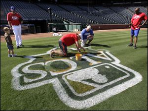 Colby Lewis and his son, Cade, left, along with Rangers first base coach Gary Pettis, right, watch as the ALCS logo is painted on the Rangers' field in Arlington, Texas.