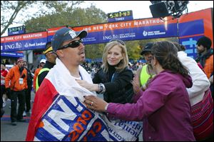 Edison Pena is greeted at the finish by Mary Wittenberg, center, New York Road Runners president, and his wife, Angelica Alvarez. Cheers prodded him on and supporters helped keep pace.