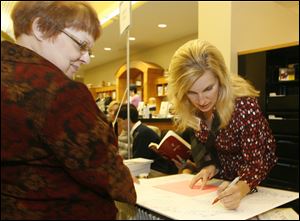 Nancy Colpaert, director of the Monroe County Library System, left, holds a signature board for author Michele Howe of La Salle, Mich., at the book fair. The library system collects the signatures of the authors who appear at the book fair. Forty participated this year.