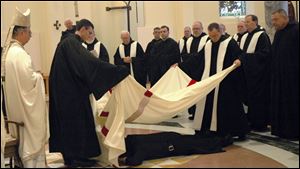 Brother Francis, prostrate on the church floor, is covered with a white-and-red pall used in monastic funerals to symbolize the death of his former self as Craig Wagner.